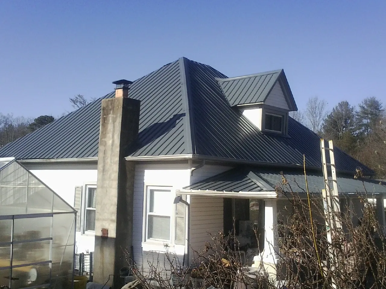 Dark blue standing seam metal roof on a white farmhouse with dormer — Slate & Tile Roof Repair by Roofing Brothers in Una