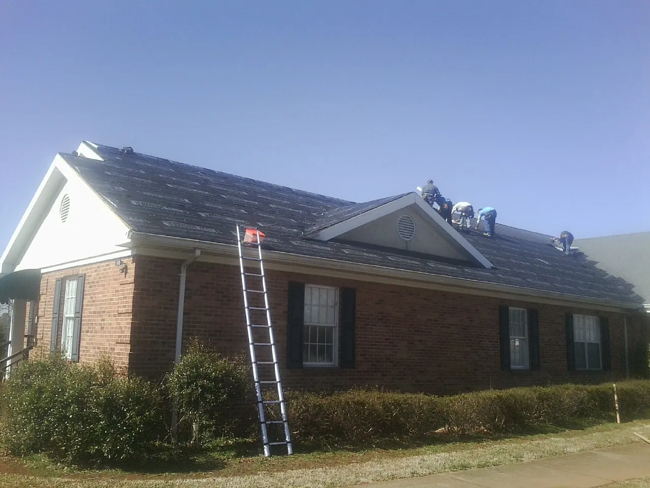 Crew tearing shingles off a brick ranch roof with a ladder set — Emergency Roof Repair work by our crew in Una