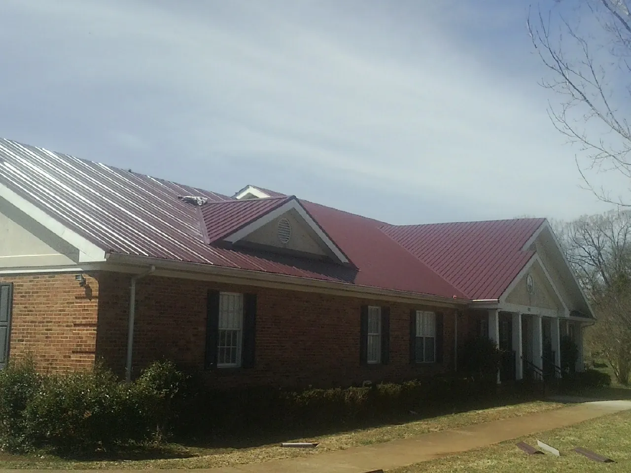 Red metal roof with gabled entries on a long brick building, from a Hail Damage Roof Repair job in Una