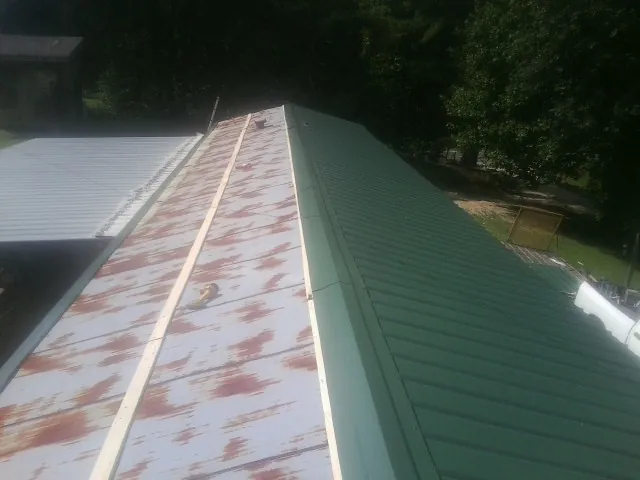 Old rusted panels beside newly installed green metal roofing — Wind Damage Roof Repair by Roofing Brothers in Una