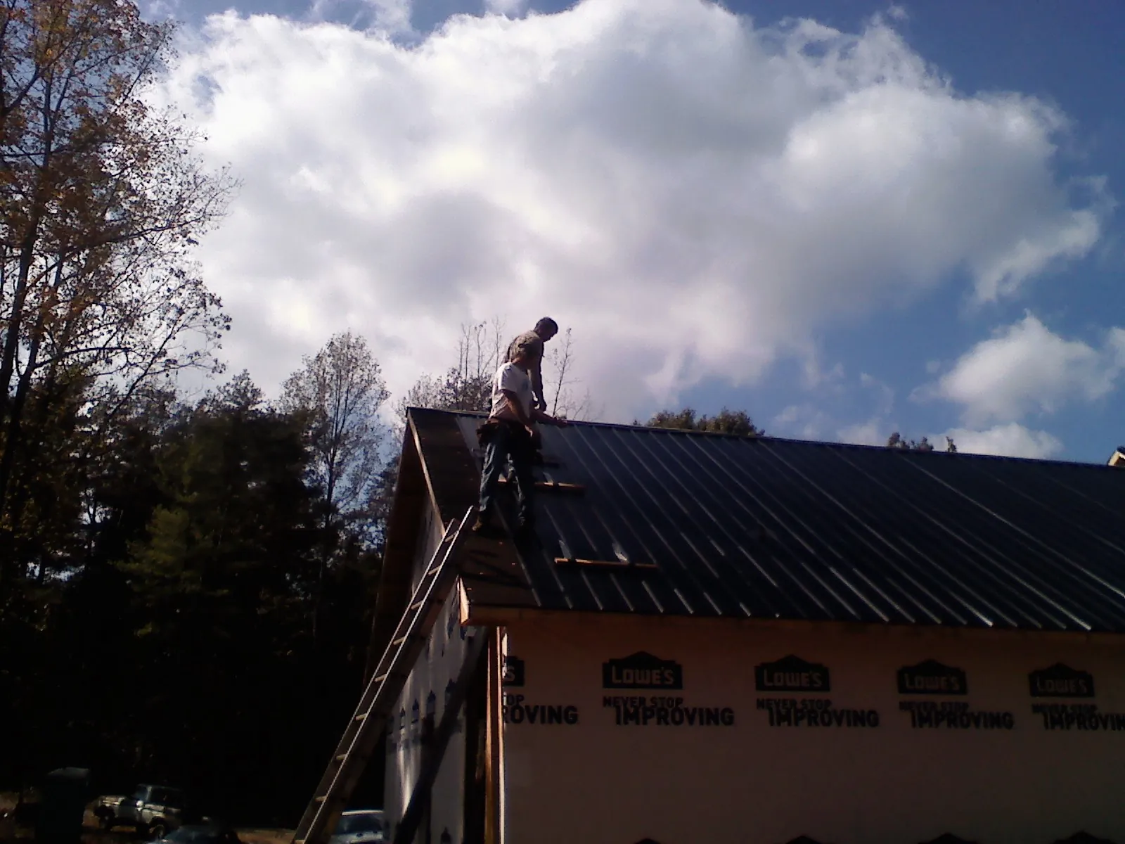 Roofer fastening dark metal panels high against a cloudy sky, from a Roof Inspection job in Una