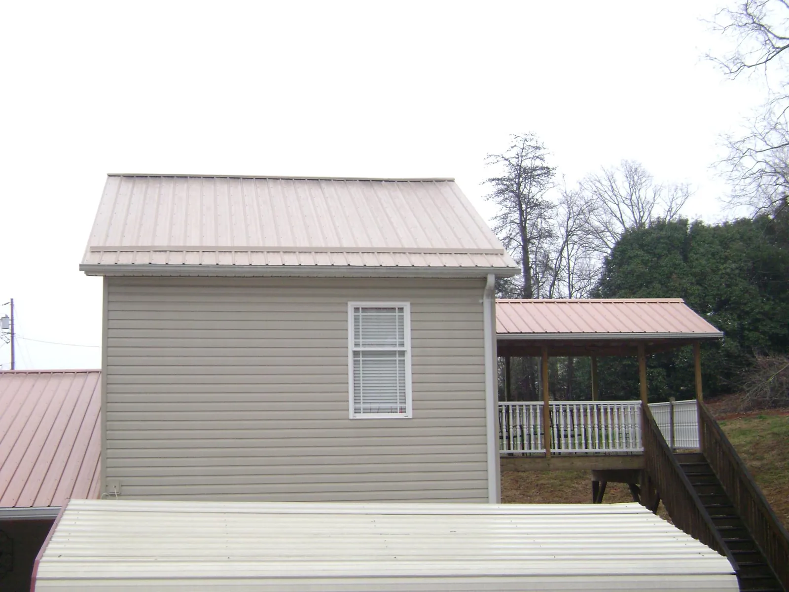 Tan metal roofs on a two story addition and attached porch, from a Roof Replacement job in Una